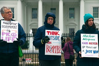 Three protesters in cold-weather gear holding placards against nuclear weapons