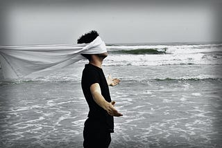 A blindfolded man attempt to look at the ocean.