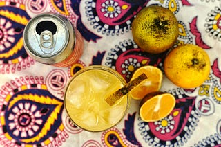 Top-down view of a can, cocktail and several pieces of fruit against a colourful pink and yellow tablecloth