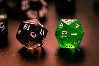 Multi-sided dice sit on a surface, a green dice and a black dice.
