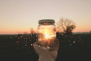 someone holding a jar of water with the sunlight and trees behind it.