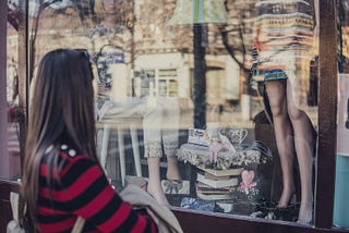 woman looking in the window of a shop that sells clothing and books