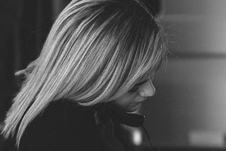 Black and white photo of blonde lady holding phone between her ear and shoulder