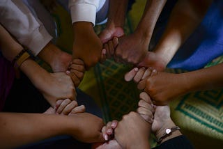 A circle of diverse hands clasped together in a powerful symbol of community, illustrating the shift from a lonely individual perspective to the strength of a collective ‘we’.