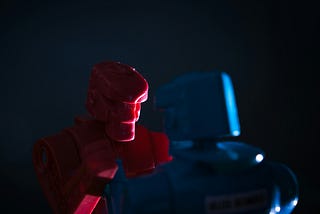 Close-up of red and blue toy robots facing each other in the dark