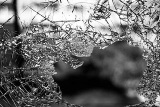 A close up black and white picture of a shattered window pane.