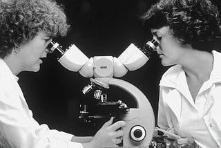 Two scientists looking into the same microscope