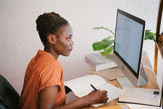 Black woman making notes while studying at a computer