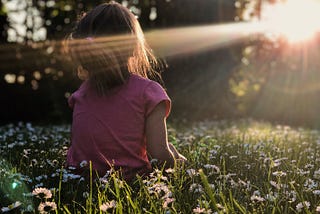 A little girl sitting on the grass enjoying the shining sun.