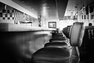 Black and white photo of the seats and counter at an American diner.