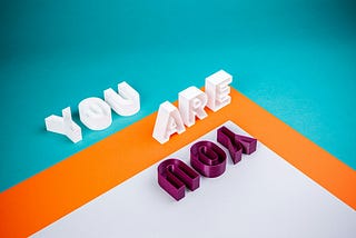 A bold graphic design with the words “You Are You.” The words tumble around part of a square (right angle) framed in orange.