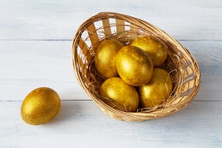 A cane basket containing golden eggs, with one outside.