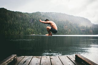 A lone man in swimming trunks jumping inside a green colored lake. There’s also plenty of fog to be seen