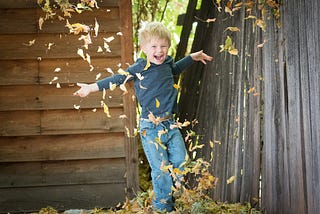 Laughing child kicking up a shower of golden crisp autumn leaves which form a heart around him