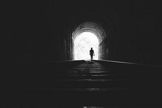 A photo of someone walking out of a dark tunnel into the light of day.