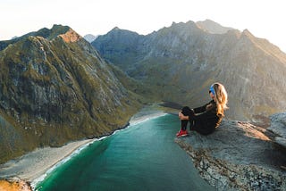 Woman sitting on edge of rock overlooking mountains and seaside
