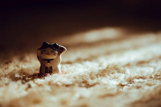 A tiny lucky cat ornament among tufts of a carpet