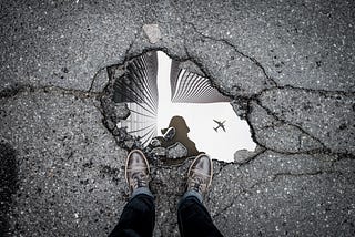 person looking at their reflection in a puddle