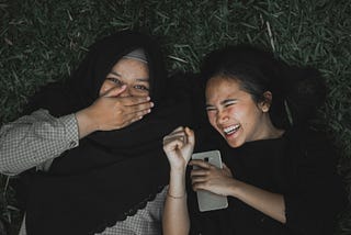 Two girls reading a message on a smartphone and laughing.