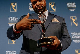 A photo of man holding up an Emmy Award.