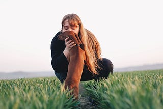 Lady kissing a dog in a green field