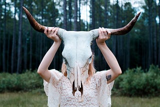 Woman in a white dress holding a ram skull