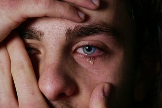 A man cradles his own face as tears flow from his eyes.