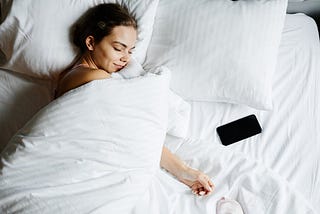 A Woman Sleeping Beside Her Smartphone. What happens when you track your sleep and run several experiments for a month to improve your recovery and sleep quality