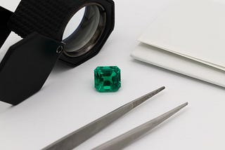A green gem with silver forceps and a magnifying glass placed on a table.