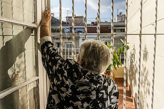 Older lady behind a barred door, looking out into the sunshine
