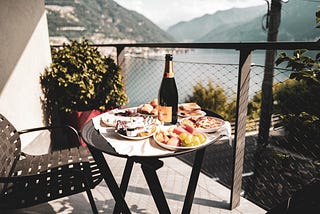 Countdown to my (2)5th Anniversary Celebration. Plates of food and wine on a small table. Balcony overlooking mountains and water.