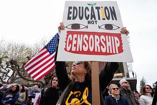 Protestors with a sign saying “Education not censorship” and an American flag