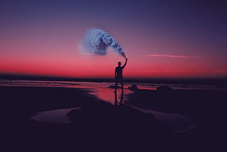 Man on a beach holding a smoke flare