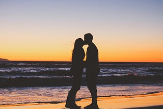 Couple kissing on the beach at sunset.