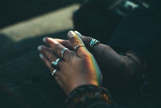 A woman clasps her hands in prayer. Silver rings adorn her fingers.