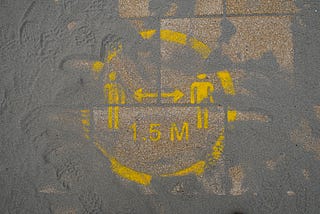 A pavement sign showing social distancing of 1.5M, covered in sand.