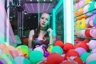Woman staring into an amusement park claw machine full of multicolored toys.