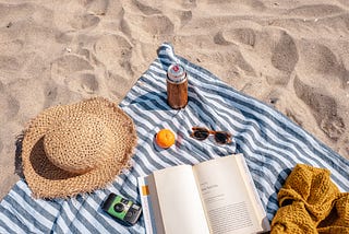 A beach towel with various items sitting on a beach.