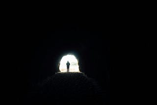 A man stading at the end of the tunnel towards the light.