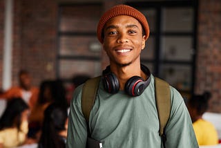 A smiling young man with headphones around his neck, in a classroom