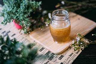 A jar of honey on a wooden board surrounded by greenery, symbolizing the richness of focus when spread thick, aligning with the metaphor of dedicating attention to fewer tasks for greater fulfillment.