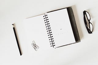 open notebook with a stack of paperclips and a pair of reading glasses