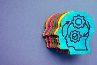 Multi-coloured wooden heads on a purple background as a symbol of diversity and inclusion. Gears and arrows on the primary head symbolize the process of unlearning.