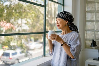 Portrait of senior Asian woman with cancer looking out window with hopeful expression