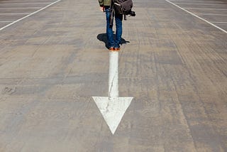 A man walking down a street with an arrow pointed backwards.