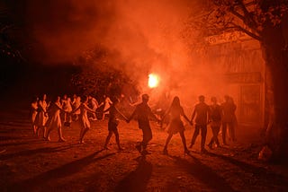 a group of revelers in a circle, hands joined, orange color palette