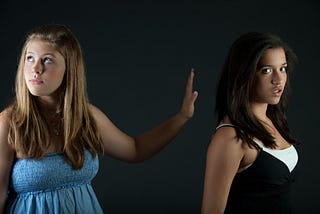 One girl holding her hand up to silence the other. Indicates bullying