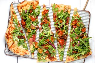 Slices of homemade pizza topped with tomatoes, vegetables, and leafy greens.