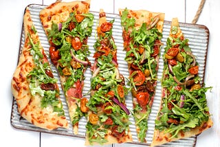 Slices of homemade pizza topped with tomatoes, vegetables, and leafy greens.