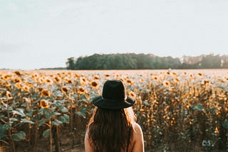Seen from behind, a woman is looking at a field of sunflowers.